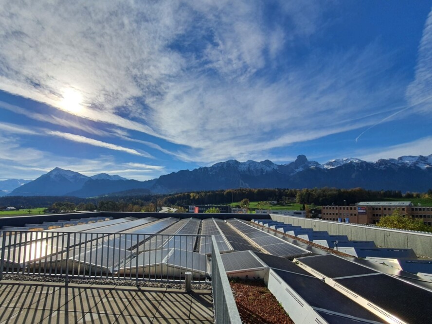 Die Solarzellen auf dem Dach des Firmengebäudes der f. zaugg ag Kälte + Klima in Thun. im Hintergrund erkennt man die Bergkette von Niesen bis Stockhorn und einen leicht bewölkten blauen Himmel.